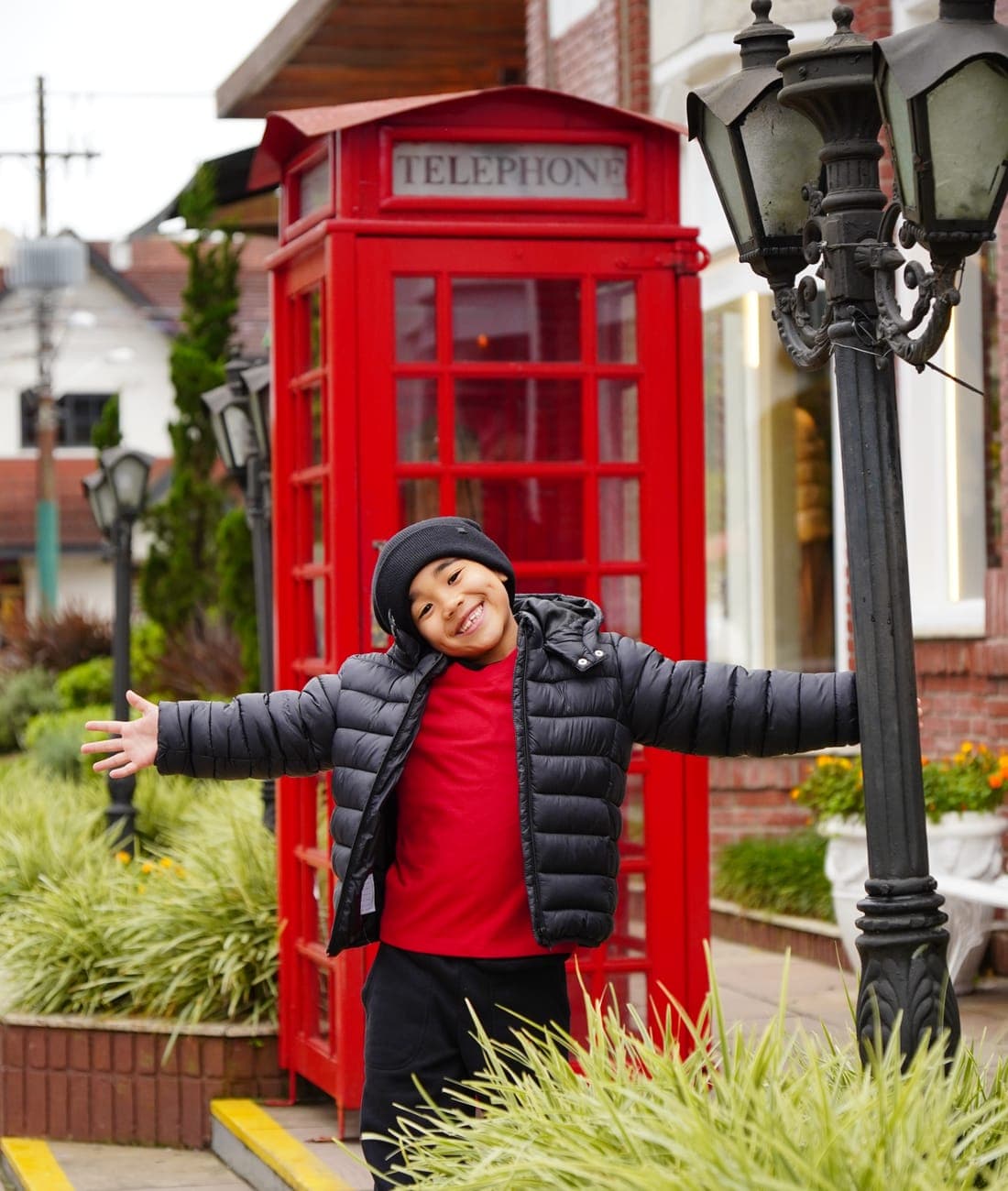 Menino sorrindo em frente à cabine telefônica vermelha do centro de Gramado